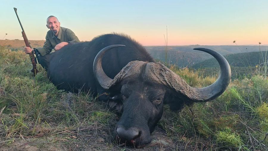 Hunter kneeling beside a trophy Cape Buffalo at sunset in South Africa